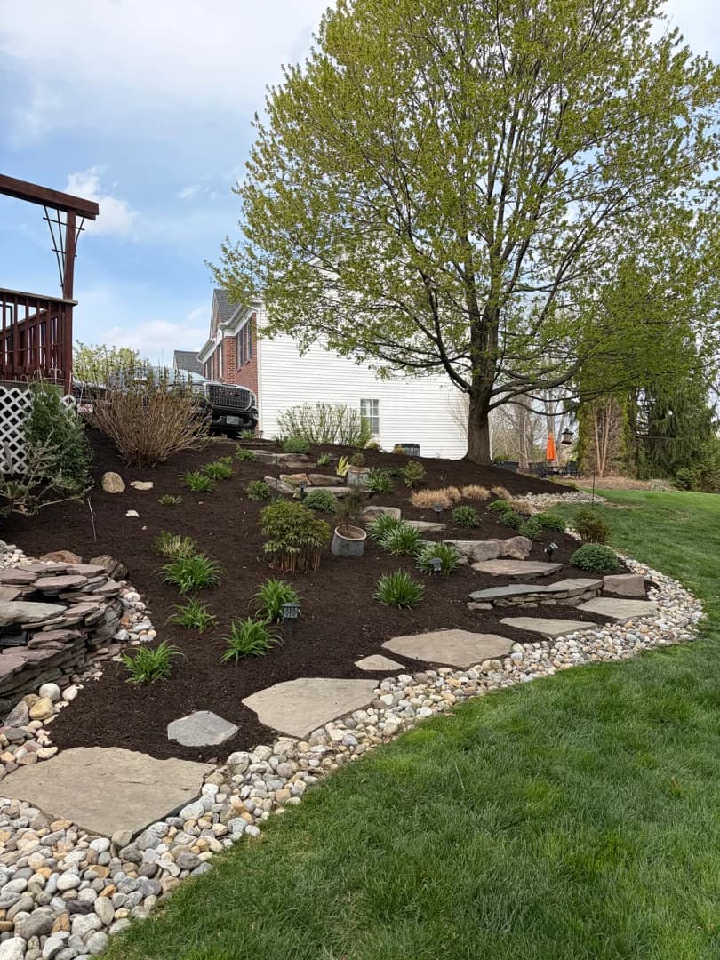 Backyard slope landscaped with fresh black mulch, river-rock border, and a natural stone stepping-stone path.