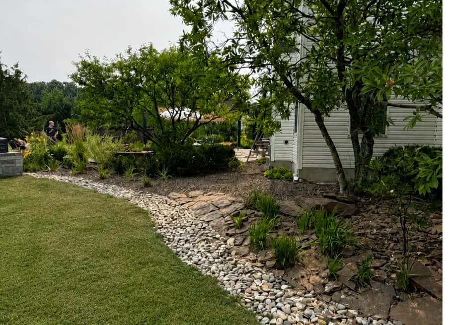 Rock bed installation with river stone and new plantings by Varsity Mulching